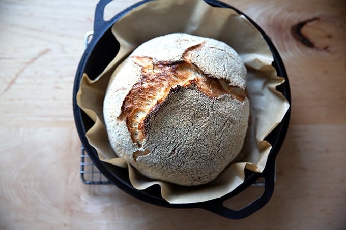 Just-baked Jim Lahey's no knead bread in a cast iron skillet on a cooling rack.