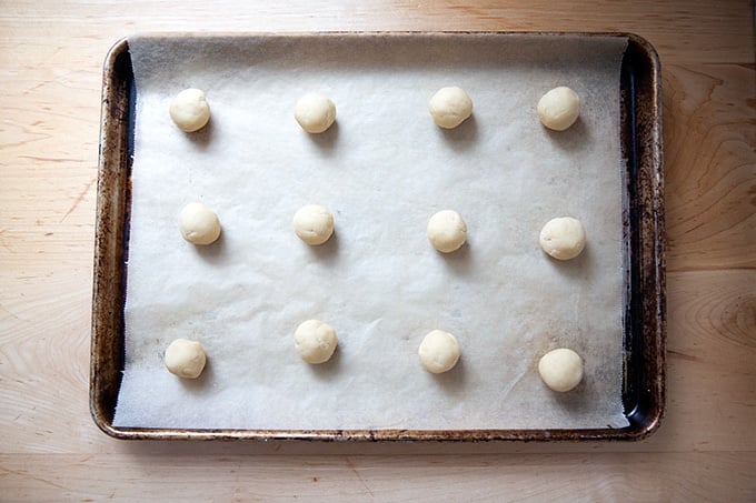 A sheet pan topped with 12 lemon-almond snowball cookie dough balls.