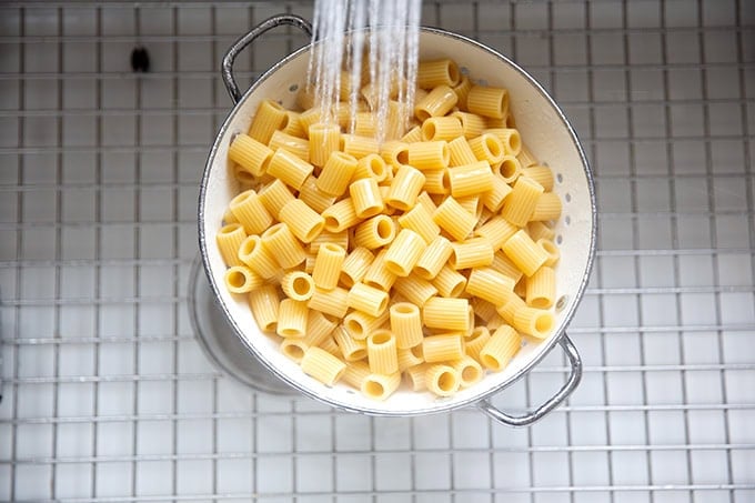 Pasta being rinsed in a colander in the sink.