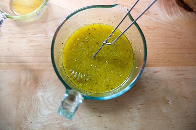 A liquid measure filled with red wine vinegar, lemon juice, salt, sugar, mustard, garlic, oregano, and olive oil all whisked together.