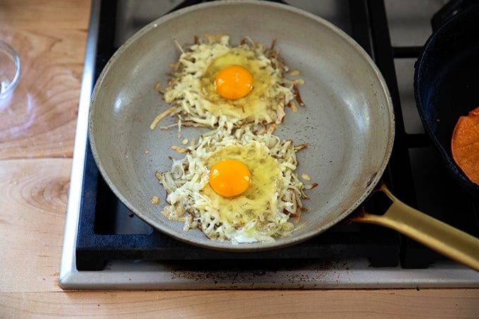 A skillet holding crispy potatoes, cheese, and uncooked eggs.