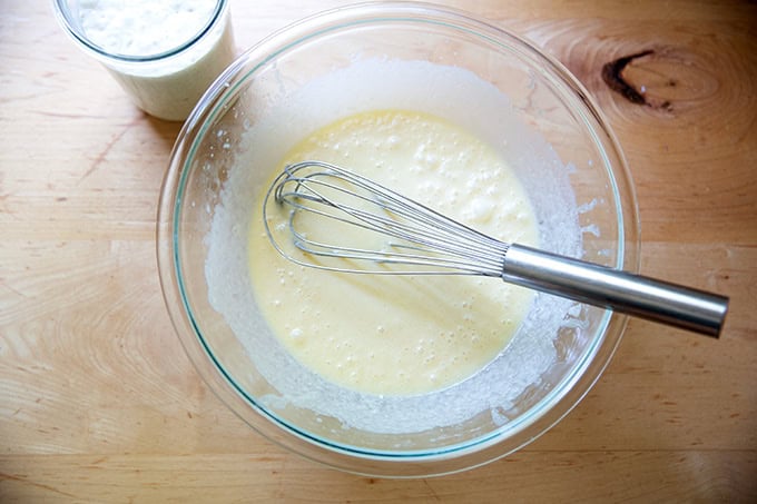 A large bowl filled with melted butter, eggs, and buttermilk all whisked together aside a container filled with sourdough discard.