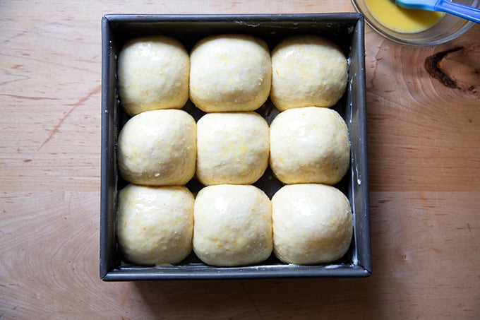 A pan of egg washed hot cross buns, ready for the oven.