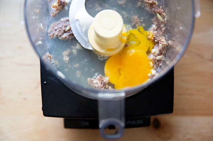 A food processor filled with puréed garlic and anchovies plus fresh lemon juice, white balsamic vinegar, and two egg whites.