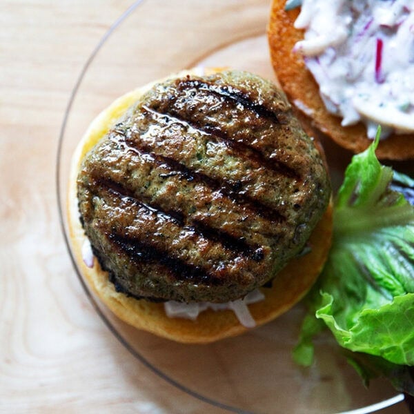A plated turkey burger aside some lettuce, bun spread with raita.