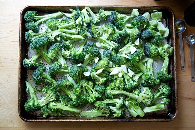 A sheet pan filled with broccoli florets, topped with sliced garlic, drizzled with olive oil, and seasoned with salt and pepper.