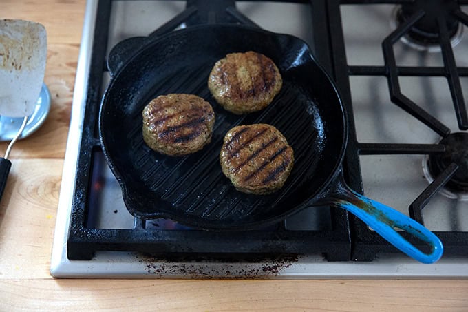Three turkey burgers cooking on a grill pan on the stovetop.