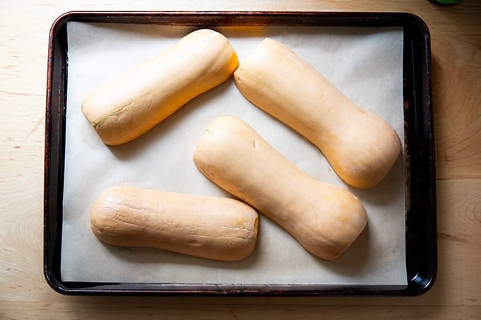 Halved butternut squash unbaked on a parchment-lined sheet pan.