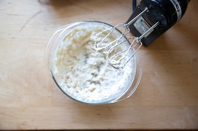 A hand-held mixer atop a bowl filled with just whipped cream cheese icing.