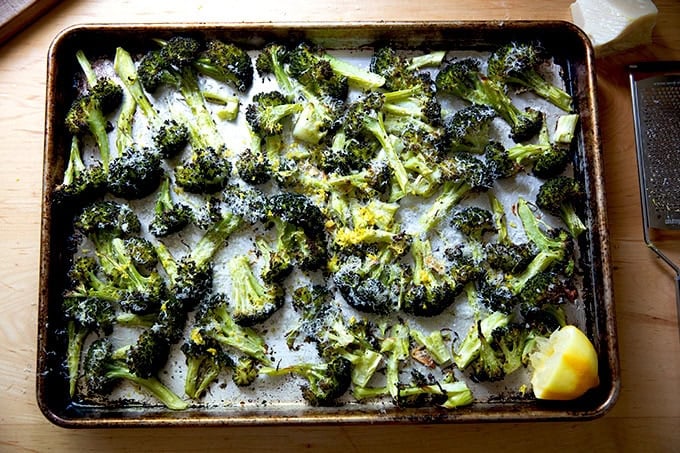 Just-roasted broccoli on a sheet pan topped with shaved parmesan, lemon zest, and fresh lemon.