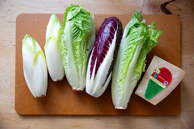 Various lettuces on a cutting board aside a wedge of Parmigiano Reggiano.