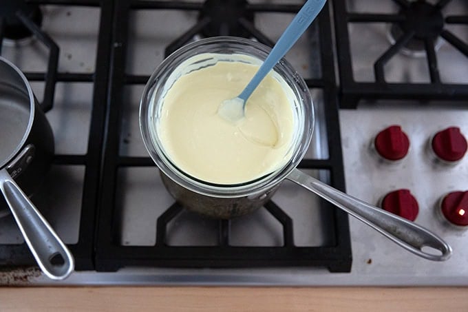 A bowl of melted white chocolate set over a pot on the stovetop.