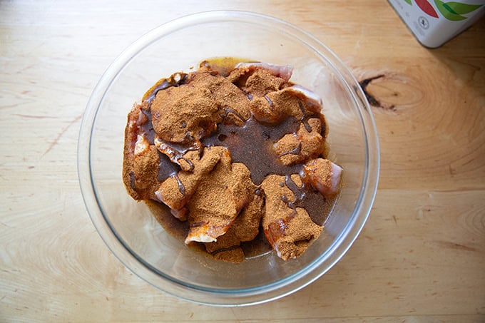 A bowl of chicken thighs covered with taco seasoning and drizzled with olive oil.