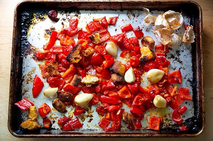 Peeled garlic cloves among other roasted vegetables to make romesco sauce on a sheet pan.