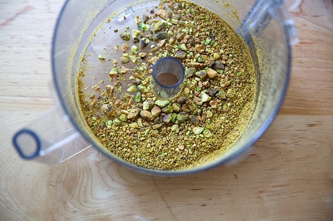 A food processor with crushed pistacios inside.
