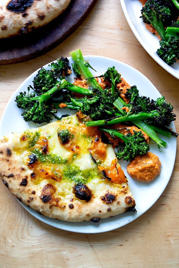 A slice of pizza aside charred broccolini on top of romesco sauce.