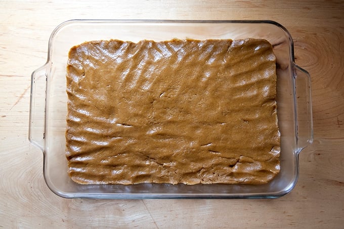 Gingerbread cookie bar batter pressed into a 9x13-inch Pyrex pan.