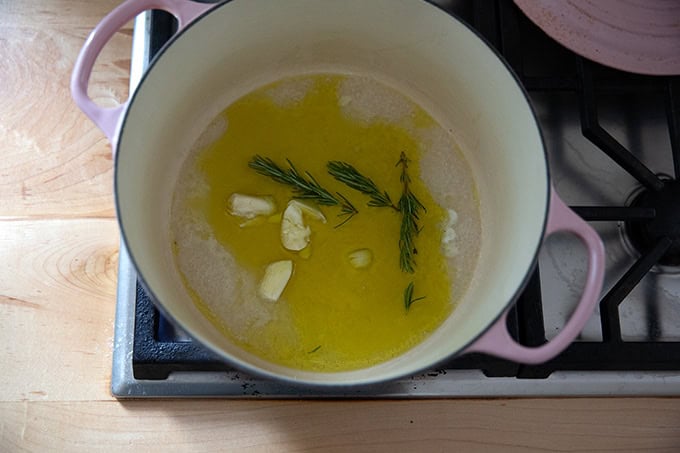 A large pot on the stovetop filled with a little bit of olive oil, water, rosemary sprigs, and garlic.