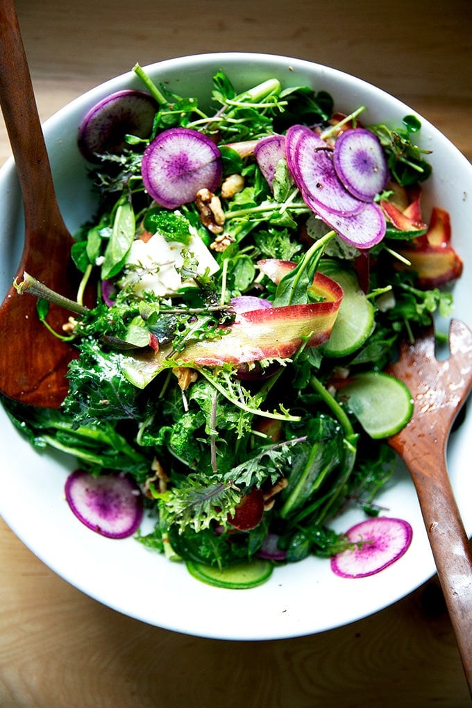 A tossed spring salad with greens, radishes, carrots, feta, and walnuts.