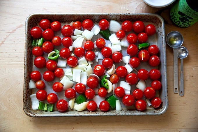 Tomatoes, garlic, chopped onions, and jalapeños on a small sheet pan tossed with olive oil and kosher salt.