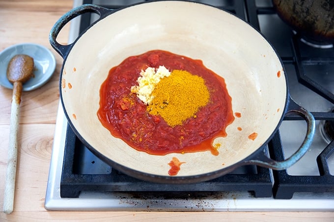 A large braising pan filled with tomatoes, curry powder, ginger, garlic, and salt.