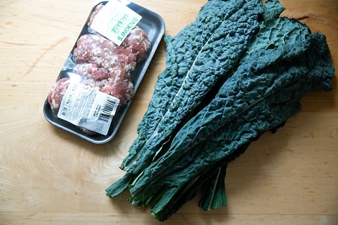 Sweet Italian sausage aside a bundle of kale on a countertop.