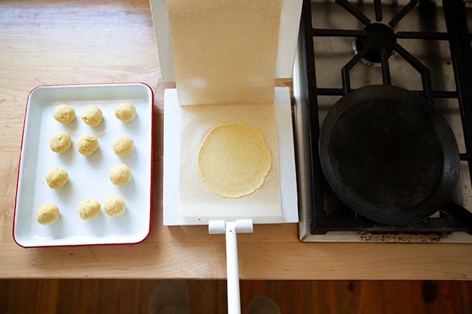 A pressed uncooked corn tortilla in a tortilla press aside a skillet.