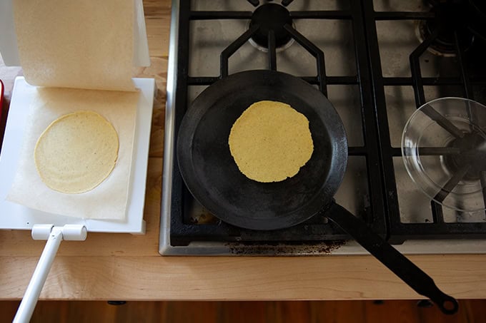 A corn tortilla cooking in a skillet on the stovetop.