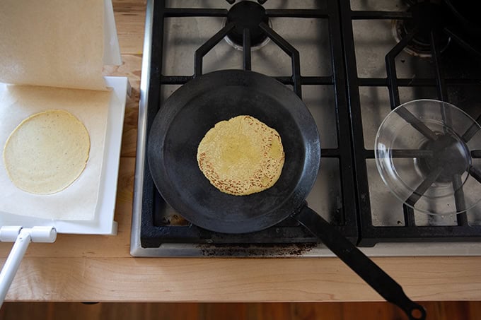 A corn tortilla cooking in a skillet on the stovetop.