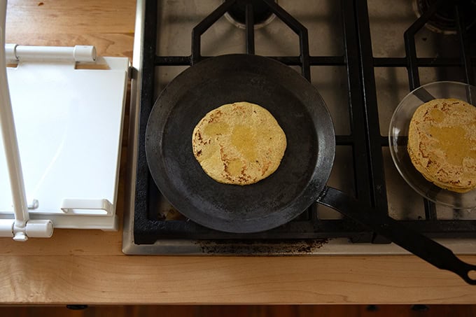 A corn tortilla cooking in a skillet on the stovetop.