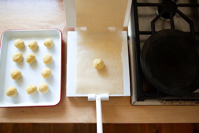 Balls of corn tortilla dough aside a tortilla press aside a skillet on a stovetop.