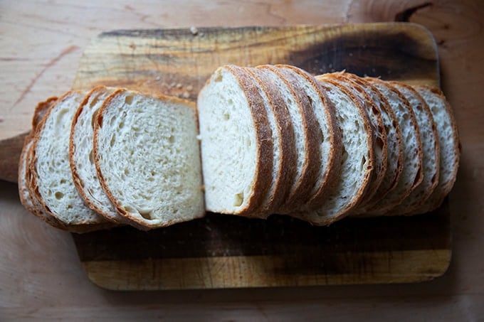 A loaf of soft sandwich bread, sliced on a cutting board.