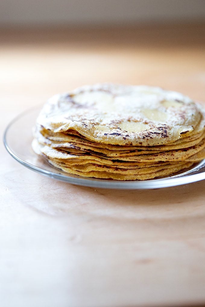 A stack of homemade corn tortillas on a plate.