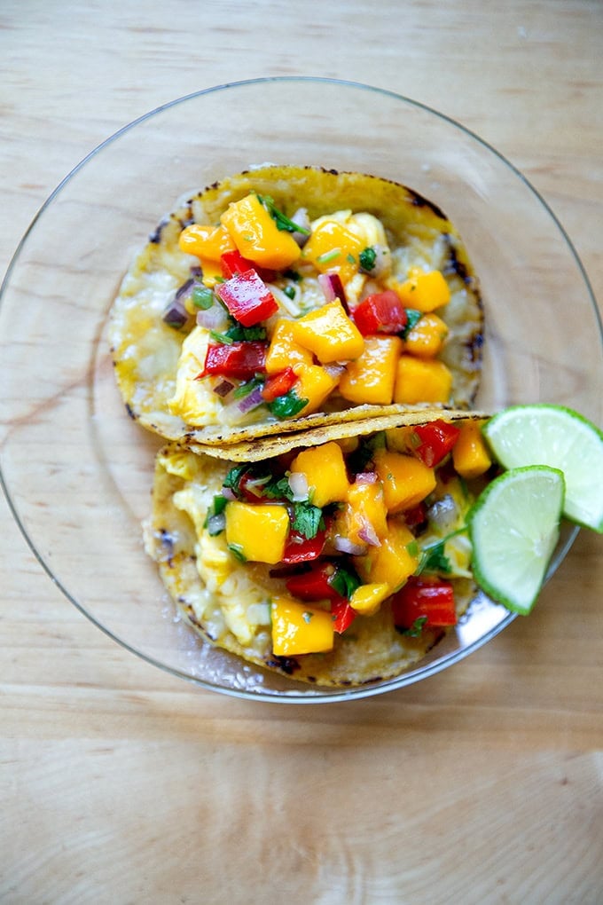 Two breakfast tacos with homemade corn tortillas filled with eggs and mango salsa.