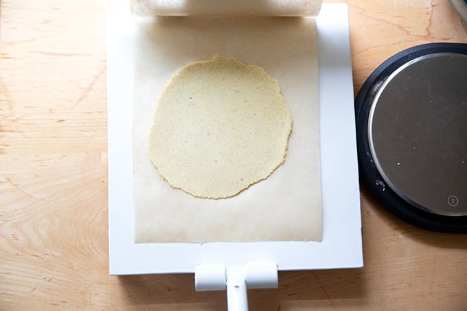 A tortilla press with a flattened tortilla in it.