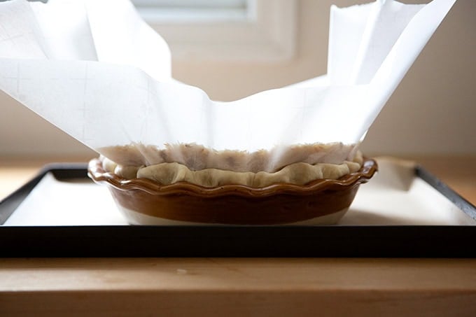 A pie plate fitted with a pie crust, lined with parchment paper and filled with pie weights.