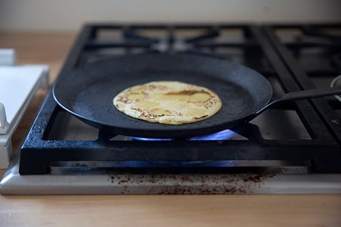 A corn tortilla cooking in a skillet on the stovetop.
