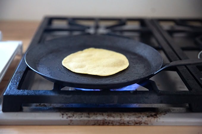 A corn tortilla cooking in a skillet on the stovetop.