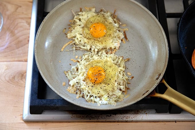 Two eggs crisping in a pan over potatoes and cheese.