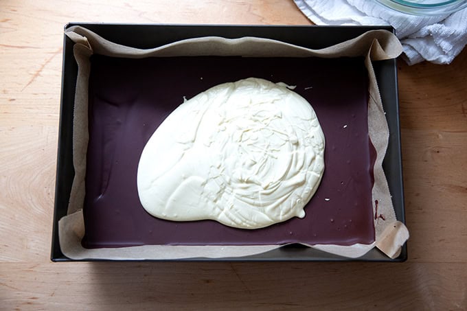 A layer of melted white chocolate not quite spread over a layer of dark chocolate in a 10x14-inch pan.