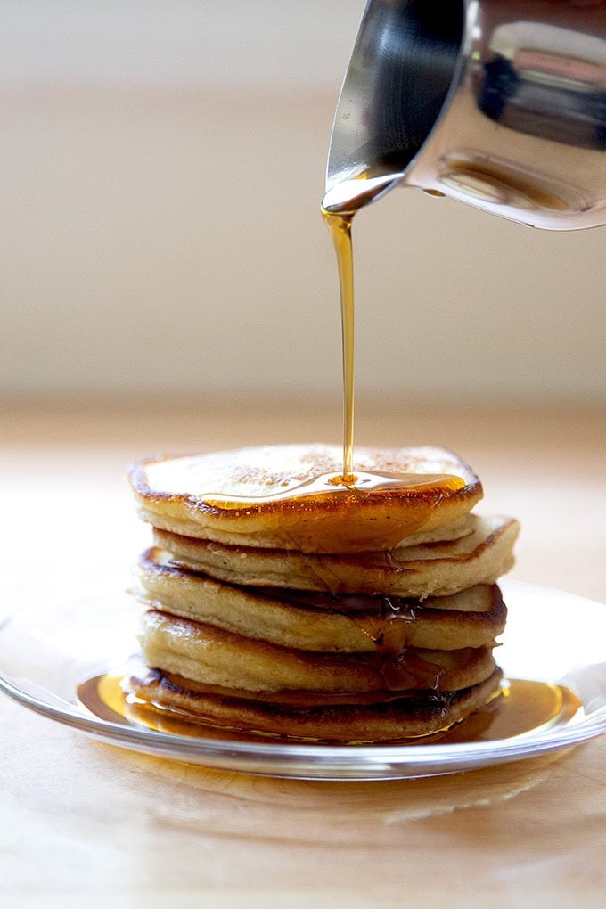 A stack of sourdough discard pancakes on a plate being drizzled with syrup.