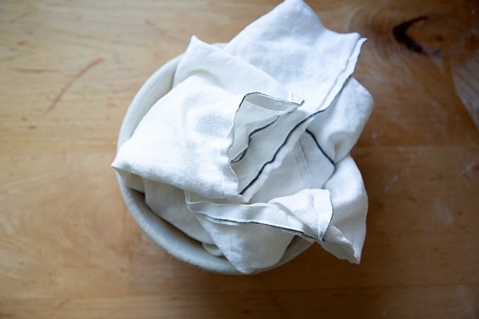 A tea towel folded over a loaf of bread dough in a banneton.