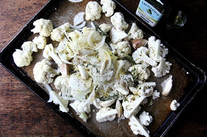 Cauliflower on a sheet pan with olive oil, salt, pepper, onions, garlic, and thyme.