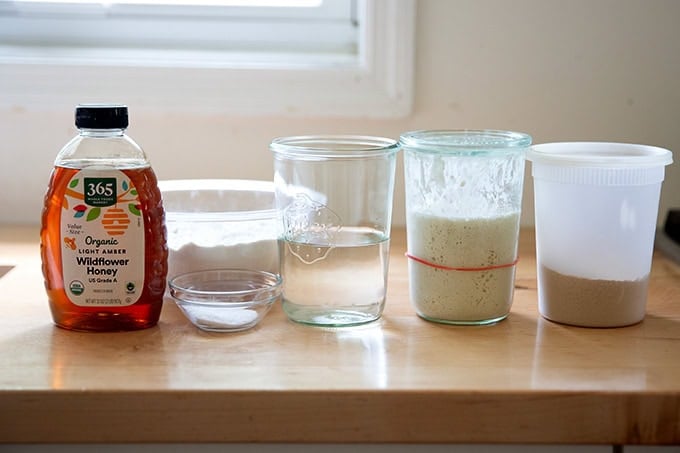 The ingredients to make sourdough discard toasting bread — honey, salt, water, sourdough discard, yeast, and flour — on a countertop.