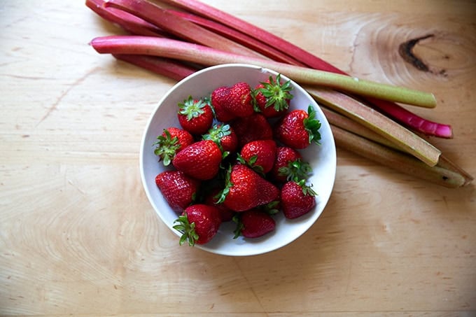 A bowl of strawberries aside a few stalks of rhubarb.