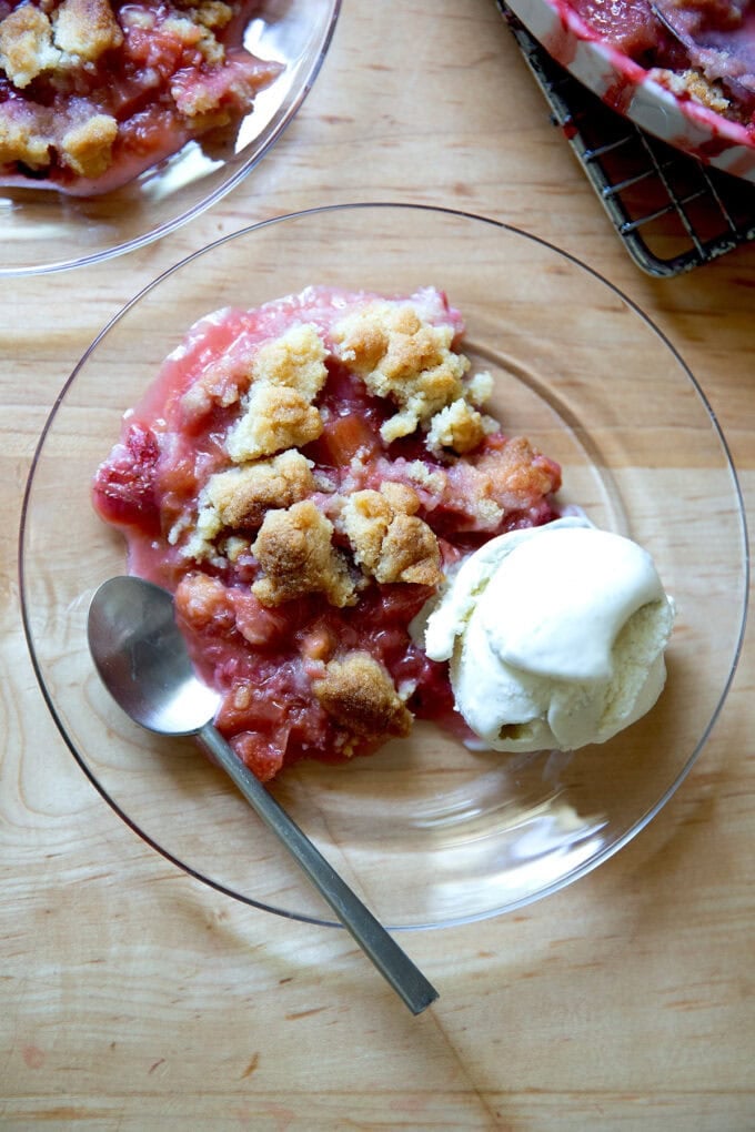 A plate of strawberry-rhubarb crisp aside a scoop of vanilla ice cream.