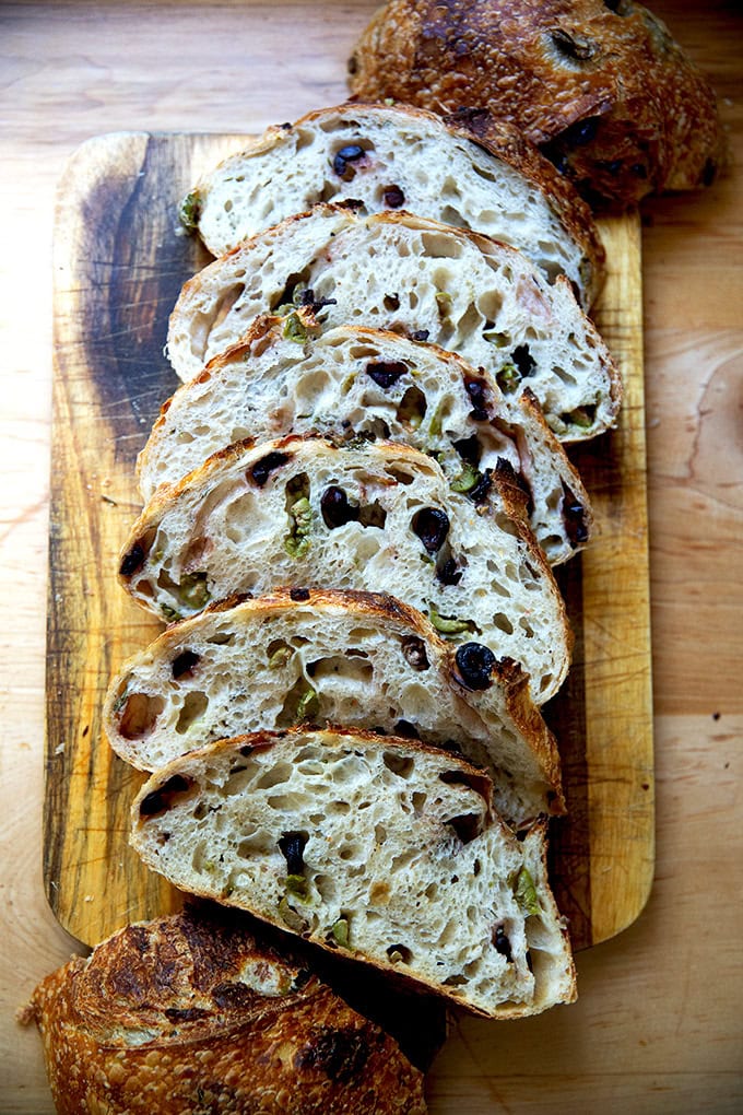A freshly baked loaf of rosemary-olive sourdough bread, sliced on a cutting board.