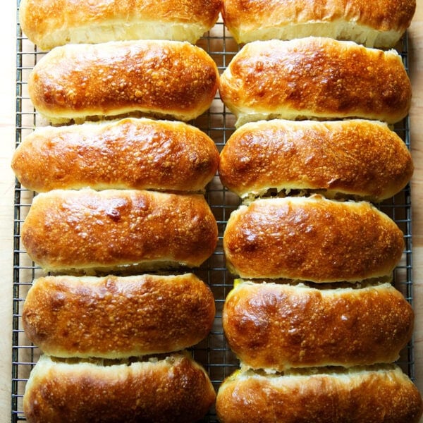 Twelve just-baked brioche hot dog buns on a cooling rack.