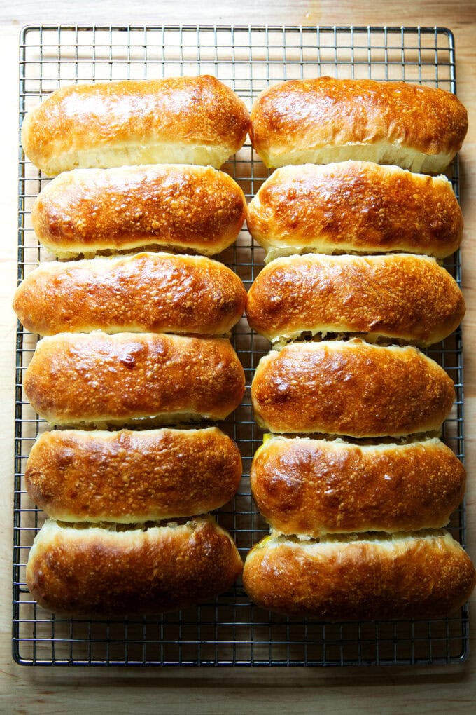 Twelve just-baked brioche hot dog buns on a cooling rack.