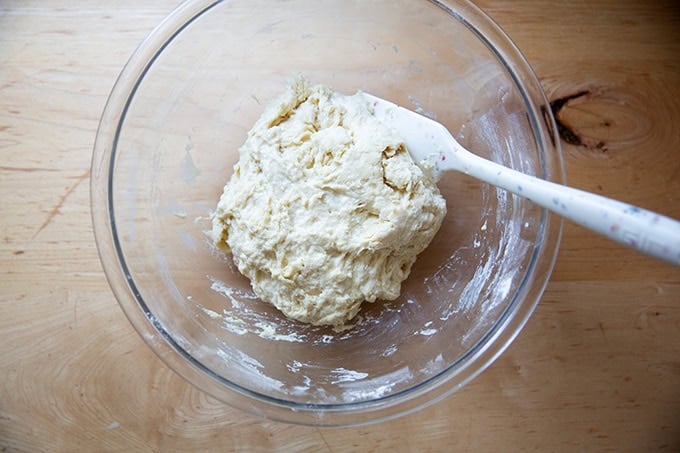 Just-mixed brioche dough in a large glass bowl with a spatula in it.
